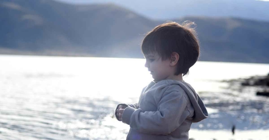 A small child standing near a lake