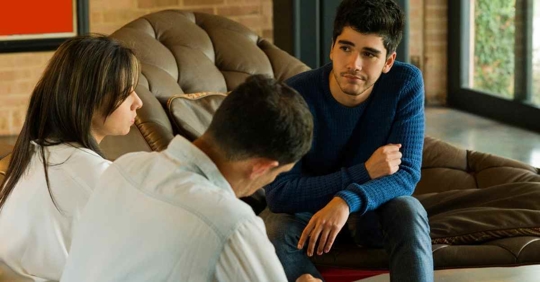 A father and mother sitting down with their son. They look like they are sharing bad news