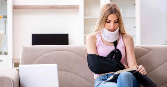 A woman wearing a neck brace and a sling over her right arm sitting on a couch