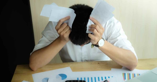 A man holding crumped papers to his head as he looks down in frustration.
