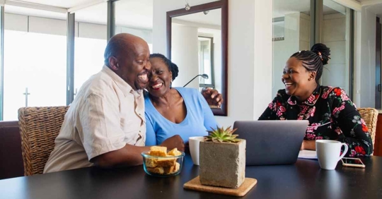 A man and woman excitedly hugging each other as they review documents with another woman