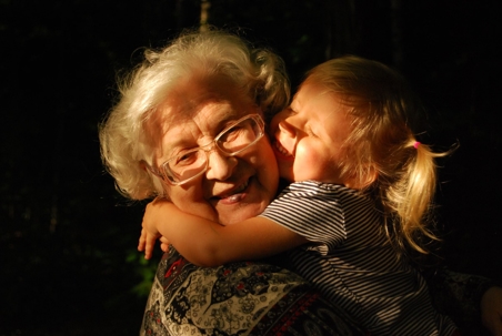 A young girl hugs her grandmother around her neck.