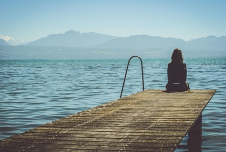 Person sits on dock looking out to a body of water.
