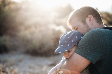 Father holds young child in an embrace outdoors.