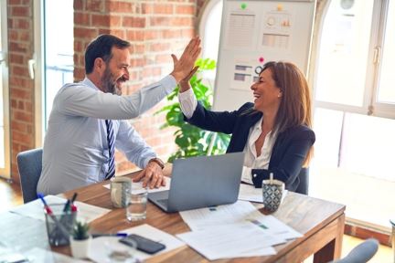 Man and woman in business attire high-five at an office desk