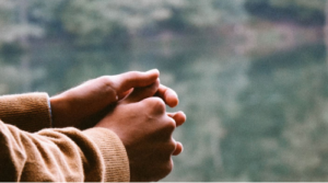 Hands gently clasped together near a window, symbolizing reflection, planning, and care for the future.