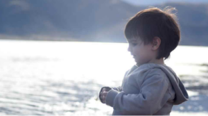 A small child standing quietly by the water, representing emotional reflection and adjustment during family changes.