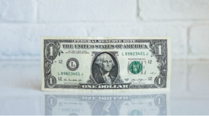 A one-dollar bill standing upright on a reflective surface.