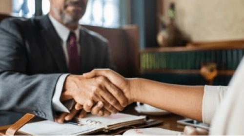 A lawyer and a client shaking hands across a desk, symbolizing trust and the start of a legal consultation.