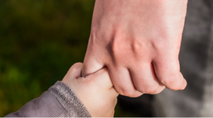 An adult holding a child&rsquo;s hand, symbolizing care, guidance, and parental responsibility.