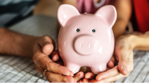 Hands holding a pink piggy bank, symbolizing saving money for child-related expenses.