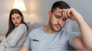 A man sitting on a couch looking stressed while a woman sits behind him appearing upset, symbolizing emotional strain during divorce proceedings.